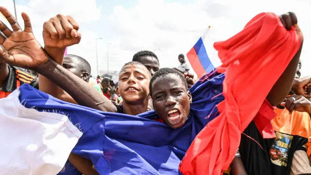 A man draped in a Russian flag waves his arms while supporters of Niger's military leaders gather for a protest outside Nigerien and French air bases in Niamey, August 27, 2023.